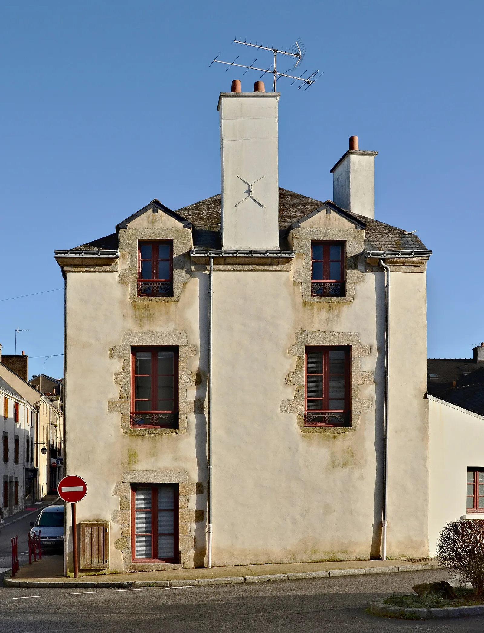 Façade enduite d'une maison ancienne en granit avec traces vertes d'humidité sous les fenêtres