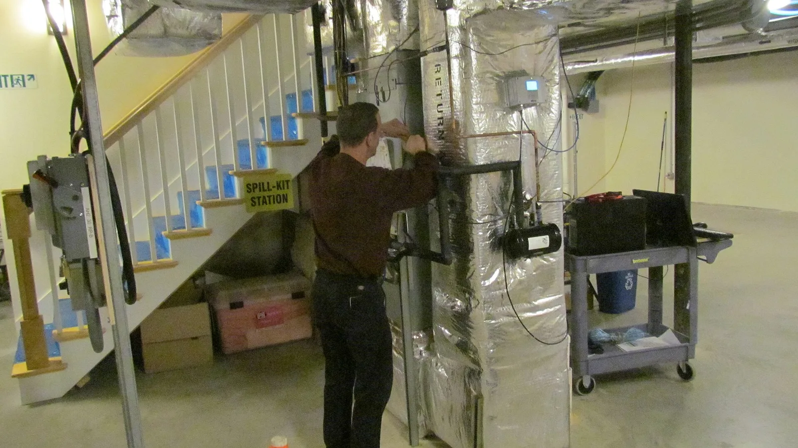 Technicien en train de poser des instruments de mesure sur une unité de pompe à chaleur et de traitement d'air installée dans un sous-sol