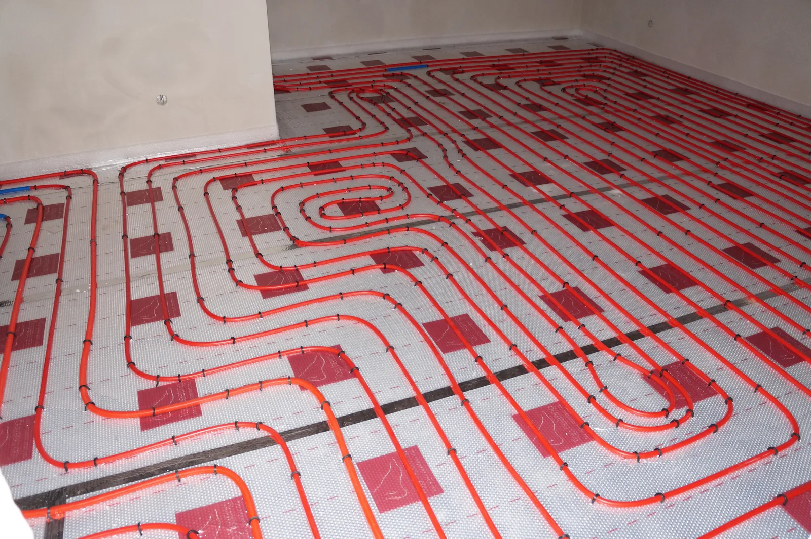 Tubes rouges de plancher chauffant à eau disposés en serpentin sur un isolant en polystyrène, avant le coulage de la chape