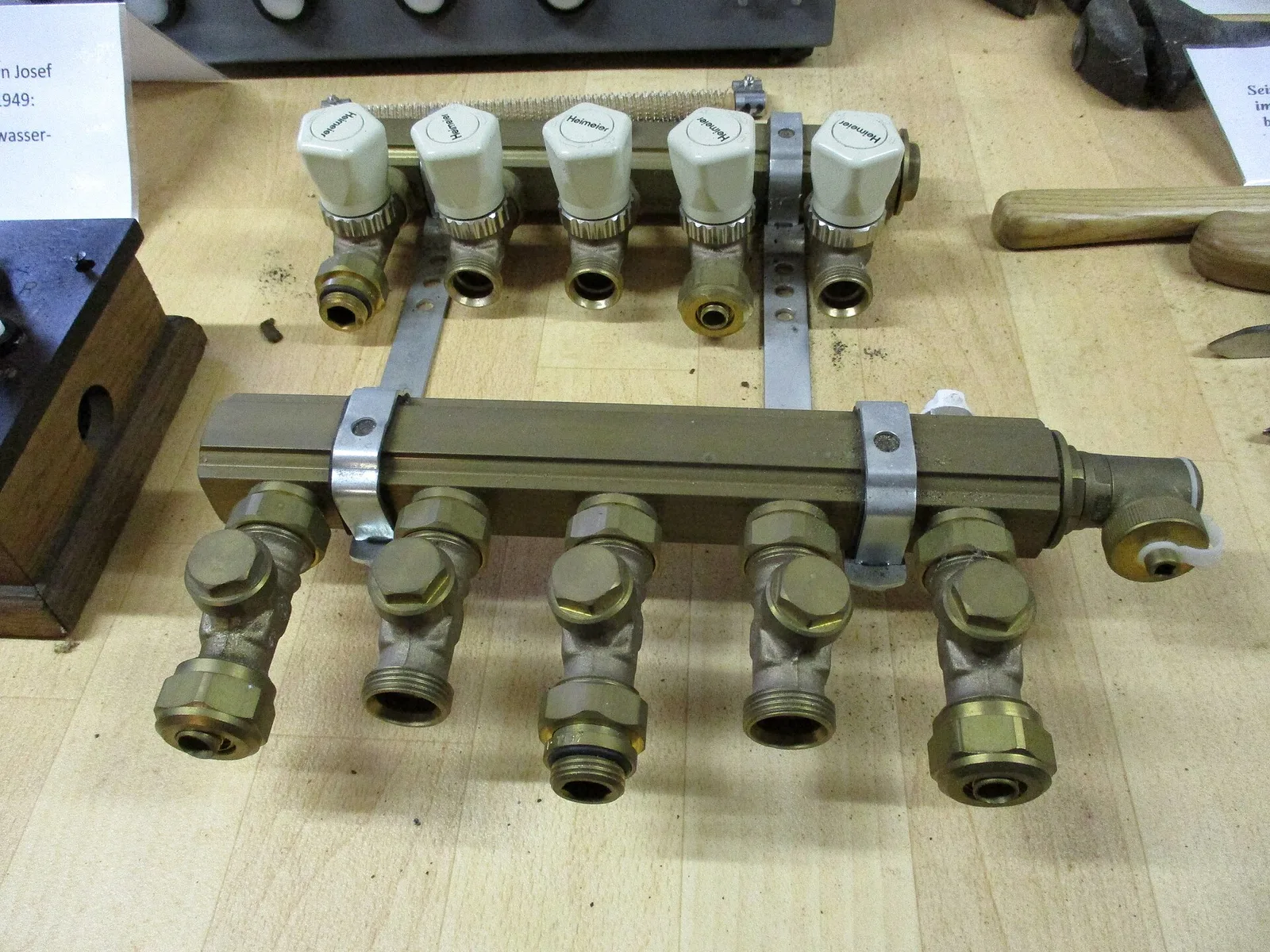 Collecteur de plancher chauffant en laiton à cinq départs, avec têtes de vannes blanches sur la barre supérieure et raccords à compression sur la barre inférieure