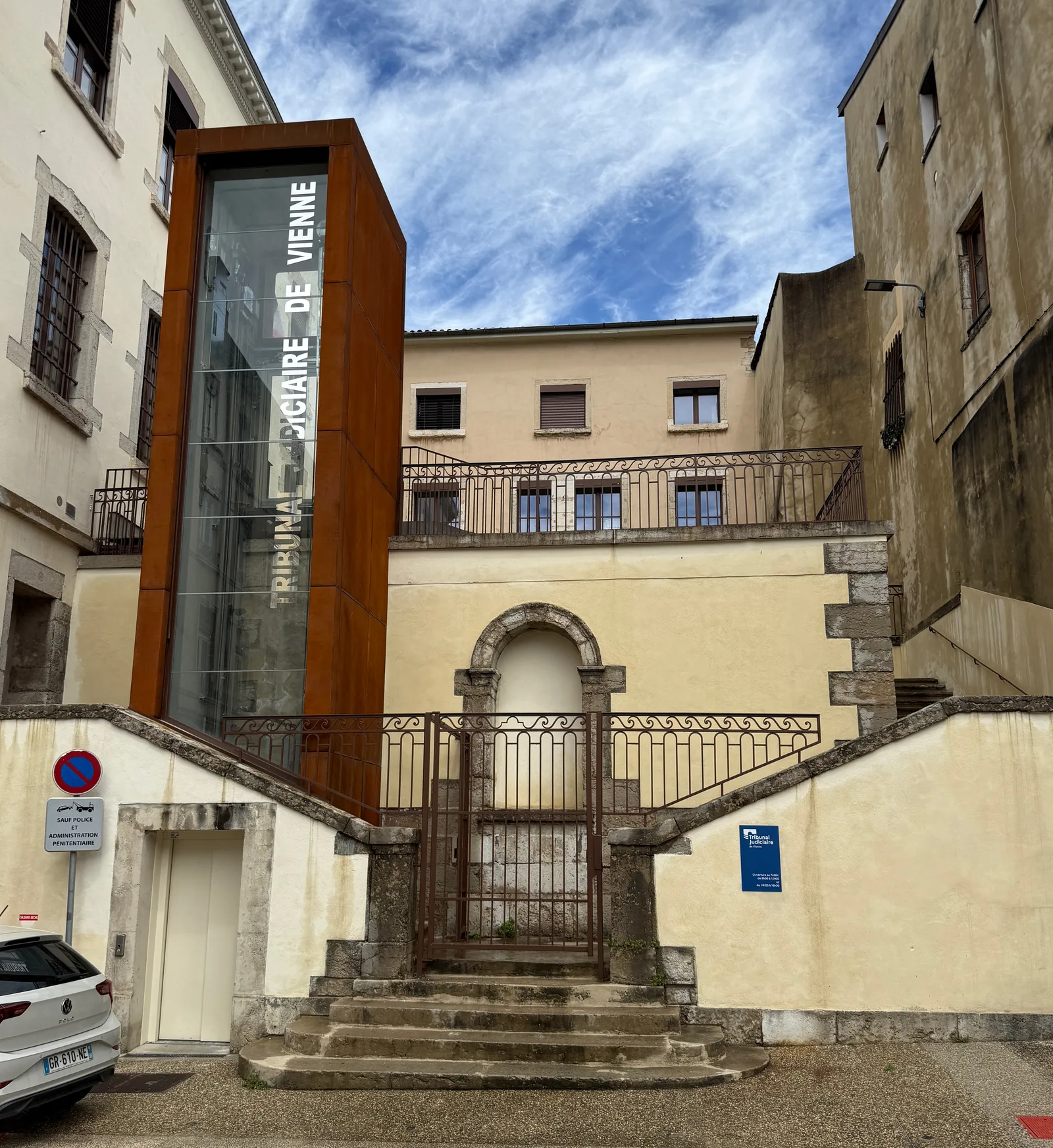 Entrée du tribunal judiciaire de Vienne en Isère, avec une tour d'ascenseur vitrée en acier corten portant le nom du tribunal et un escalier en pierre