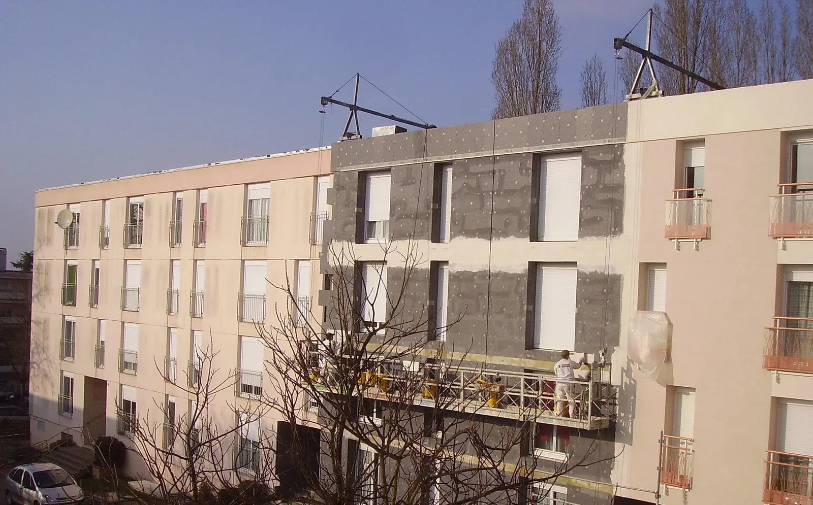 Ouvrier sur une nacelle suspendue appliquant un enduit sur des panneaux isolants fixés à la façade d'un immeuble