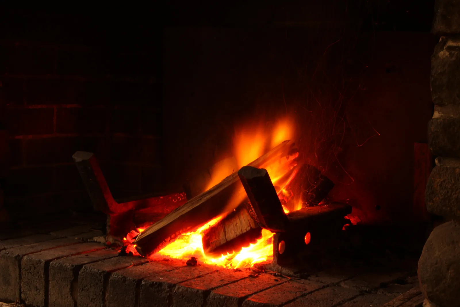Feu de bûches dans un foyer ouvert en briques, sans vitre ni porte, flammes et braises visibles