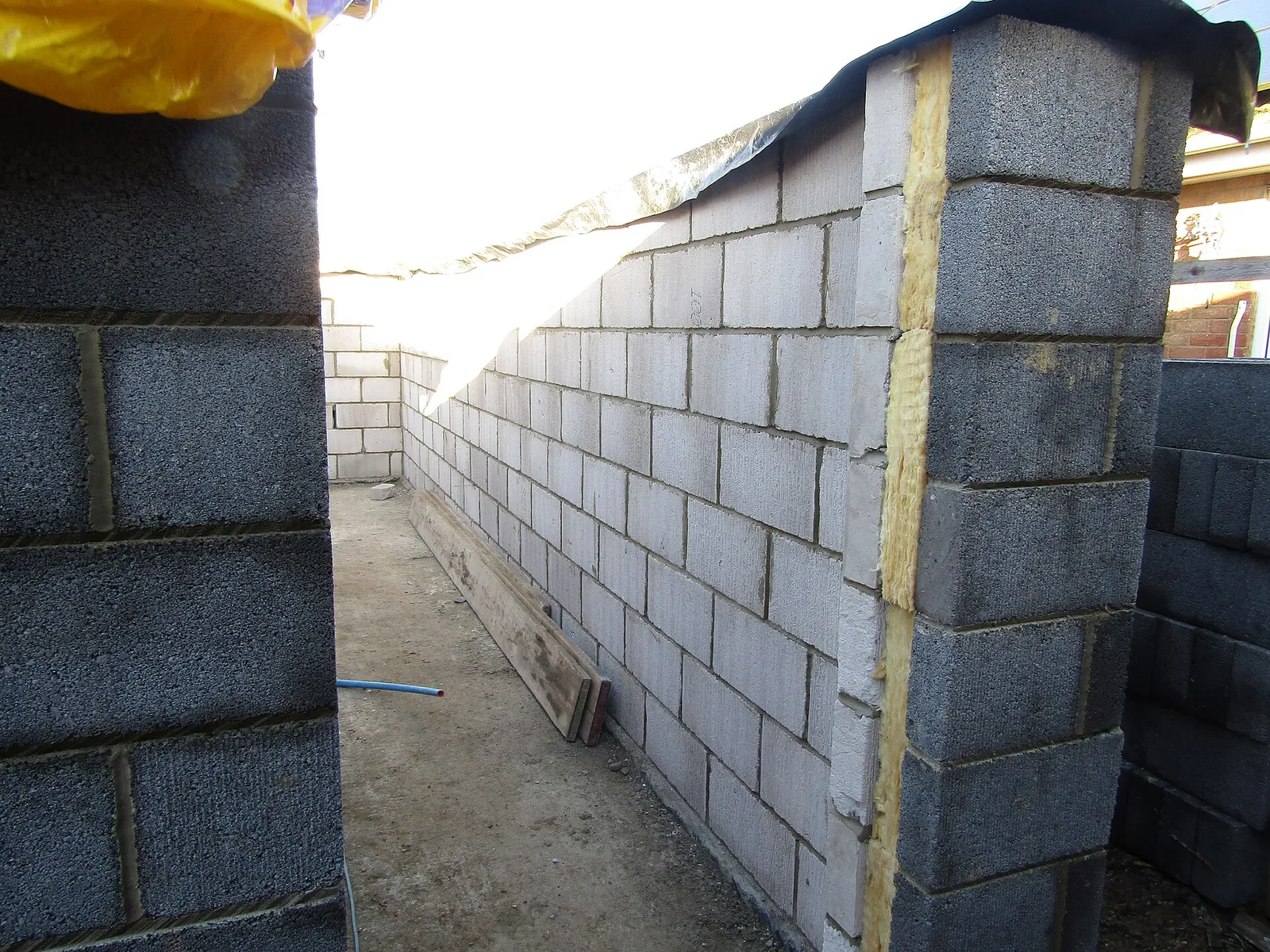 Chantier d'un mur à double paroi en blocs de béton avec une bande d'isolant jaune dans la lame d'air