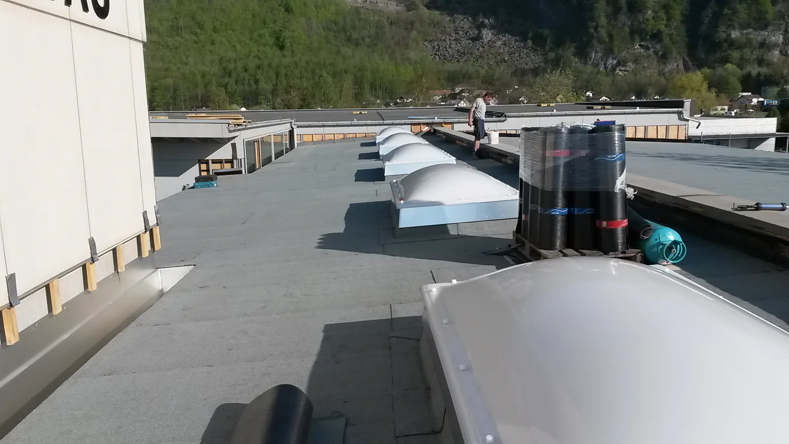 Chantier de réfection d'une grande toiture-terrasse avec rouleaux de membrane bitumineuse et lanterneaux en place