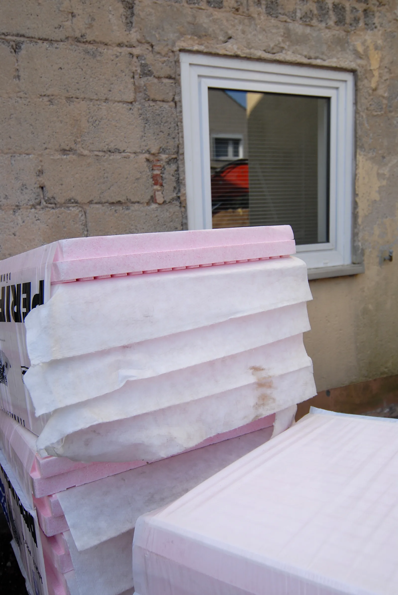 Panneaux d'isolant empilés devant une fenêtre neuve sur un mur de parpaings en cours de rénovation