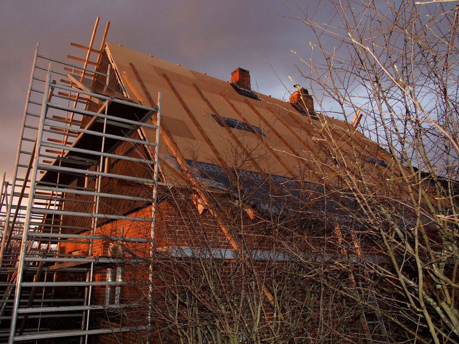 Toiture d'une maison en brique recouverte de panneaux de fibre de bois couleur ocre avant la pose des tuiles, avec un échafaudage sur le pignon