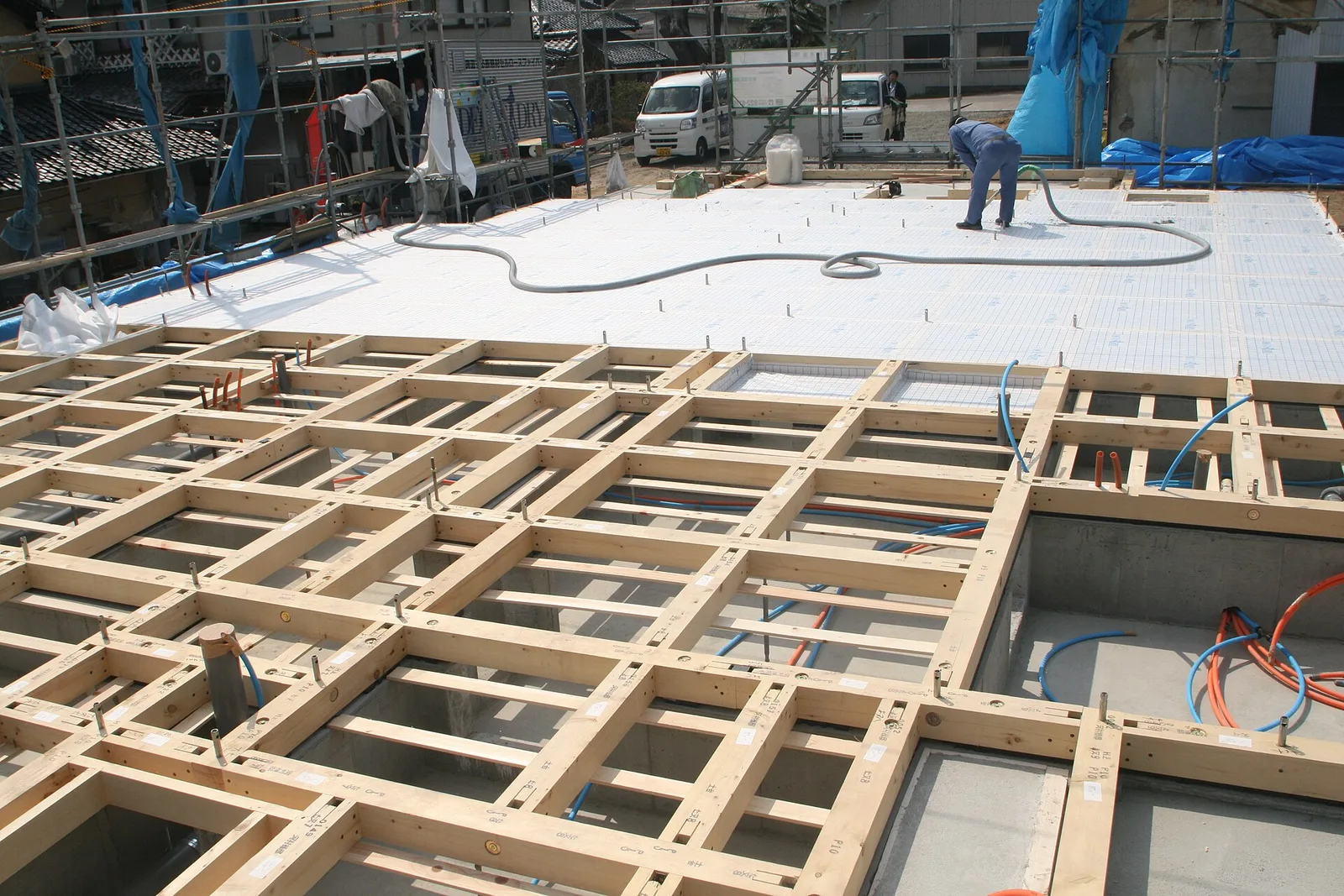 Ouvrier soufflant de la ouate de cellulose avec un long tuyau sur un plancher en panneaux pendant la construction d'une maison à ossature bois