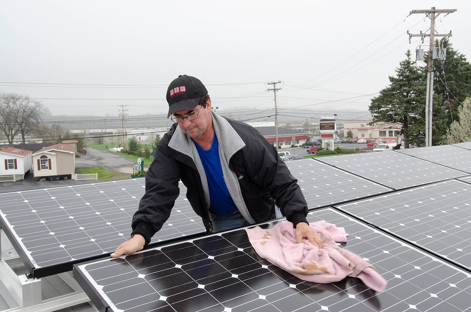 Homme qui essuie un panneau photovoltaïque avec un chiffon doux sur une installation inclinée posée sur un toit plat