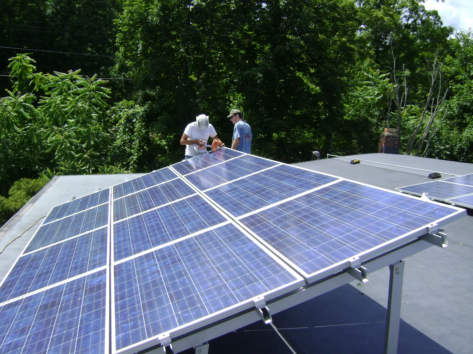 Deux techniciens fixant des panneaux photovoltaïques sur un support incliné posé sur un toit plat