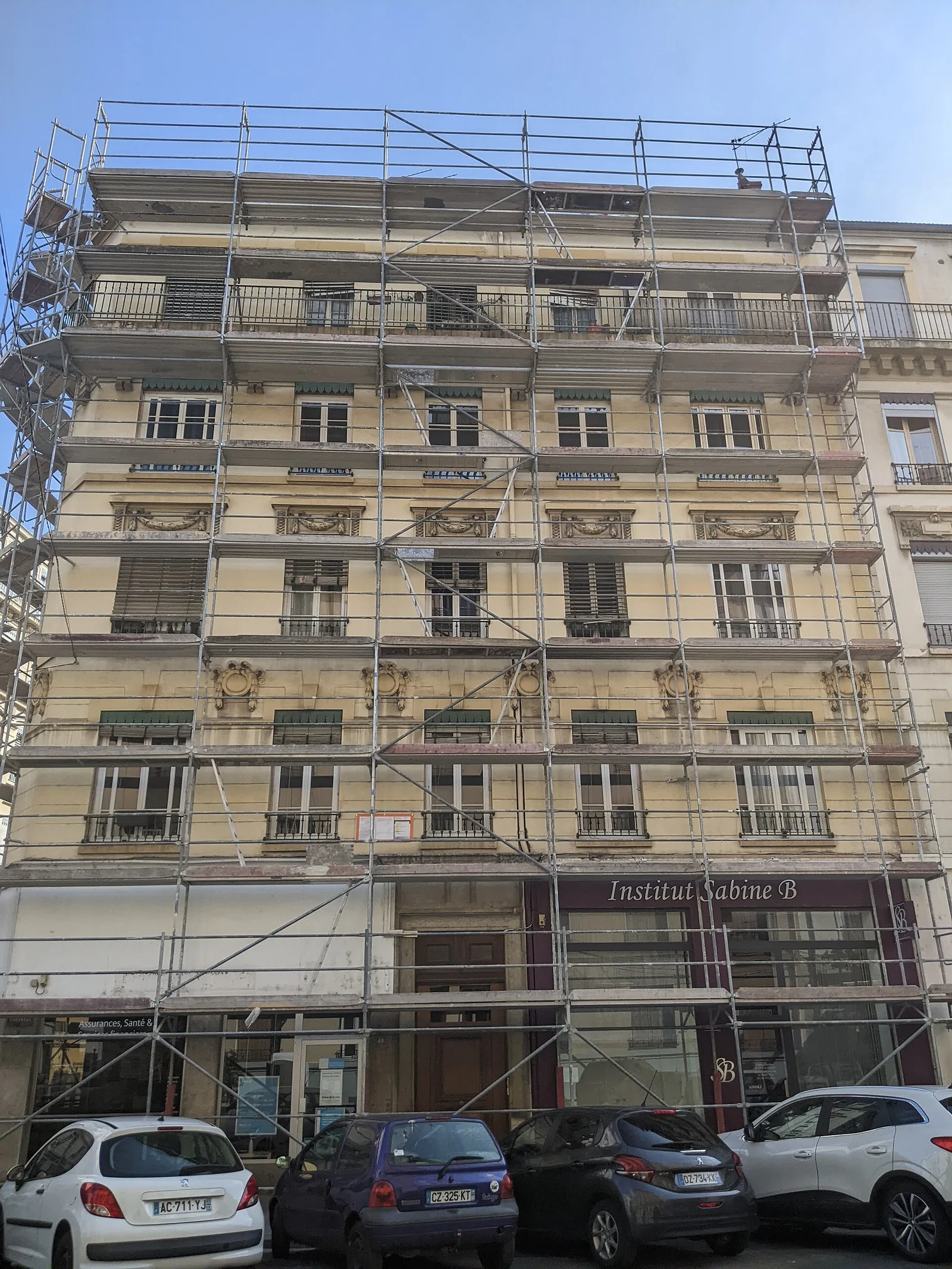 Immeuble ancien de cinq étages entièrement couvert d'échafaudages pour un ravalement de façade, rue Chevreul à Lyon, commerces au rez-de-chaussée