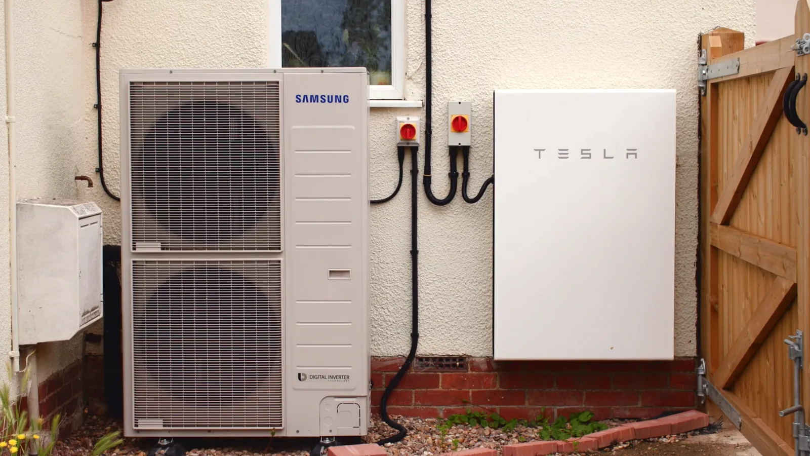 Unité extérieure d'une pompe à chaleur Samsung à double ventilateur fixée contre la façade d'une maison, à côté d'une batterie murale