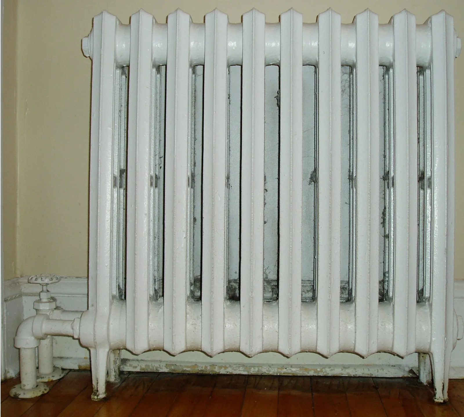 Radiateur en fonte à colonnes peint en blanc, avec son robinet manuel en bas à gauche
