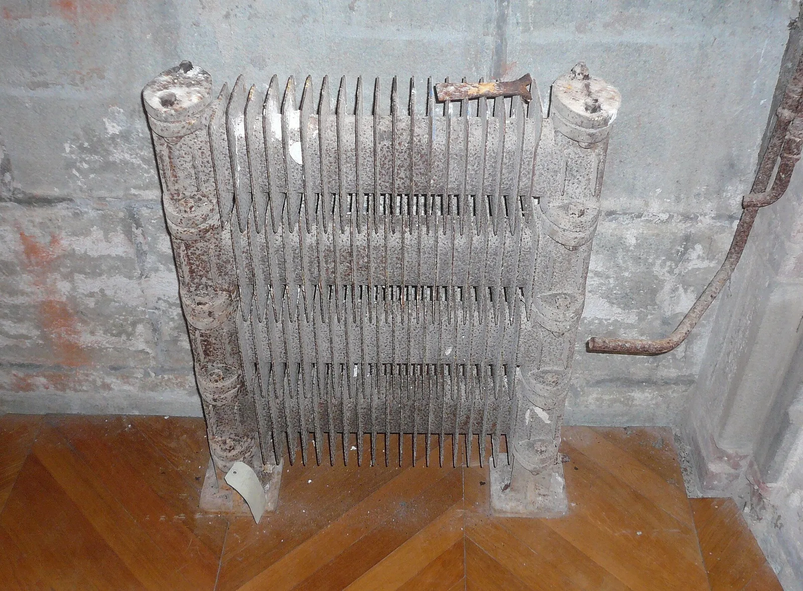 Ancien radiateur à ailettes rouillé, sans plaque d'identification visible, posé sur un parquet