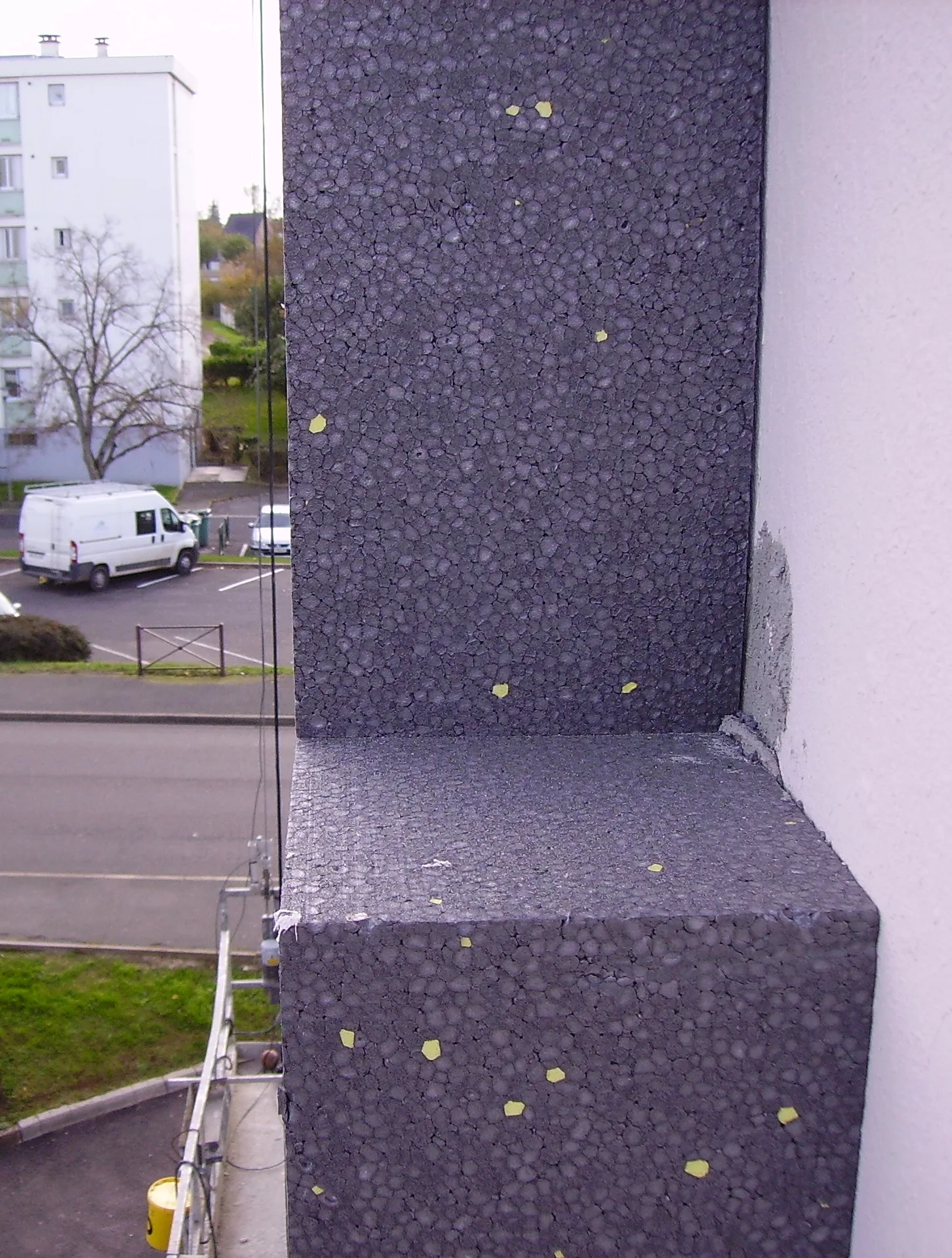 Panneaux isolants en polystyrène gris graphité collés sur la façade d'un immeuble, avec un angle d'ouverture de fenêtre