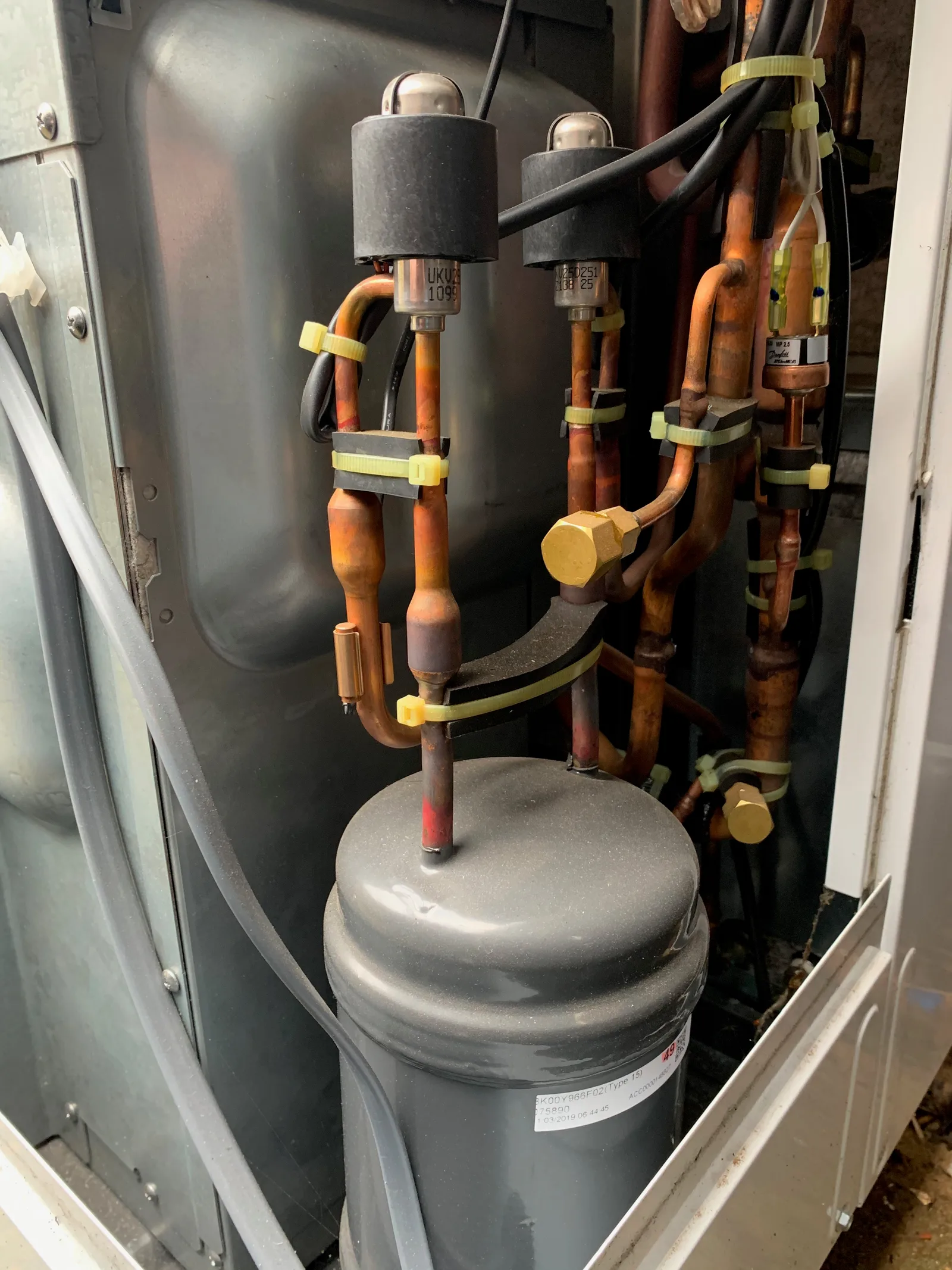 Intérieur d'une unité extérieure de pompe à chaleur air-eau : compresseur, détendeurs et tuyauteries en cuivre