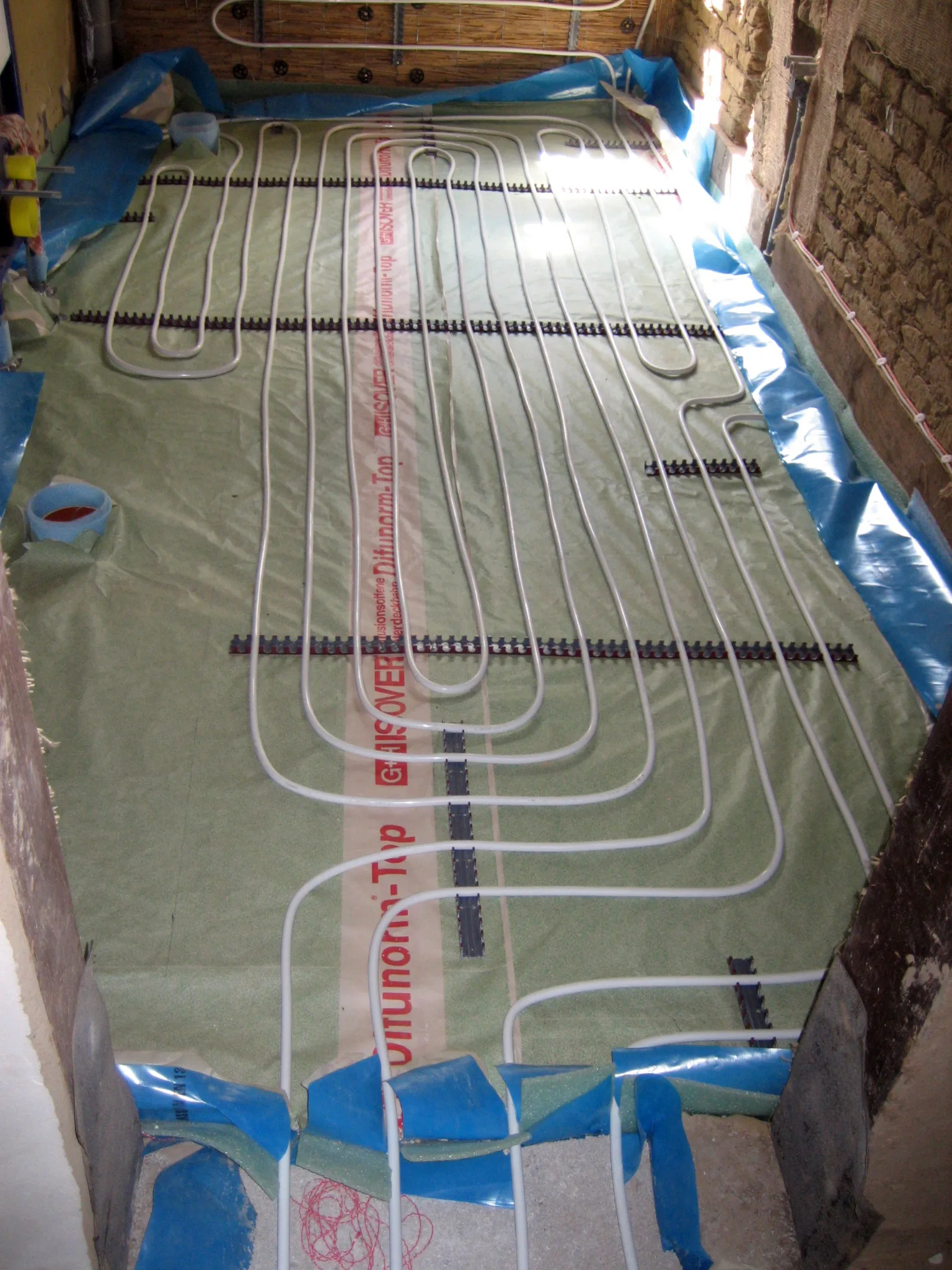 Tubes de plancher chauffant en cours de pose en serpentin sur isolant, dans une maison ancienne en rénovation