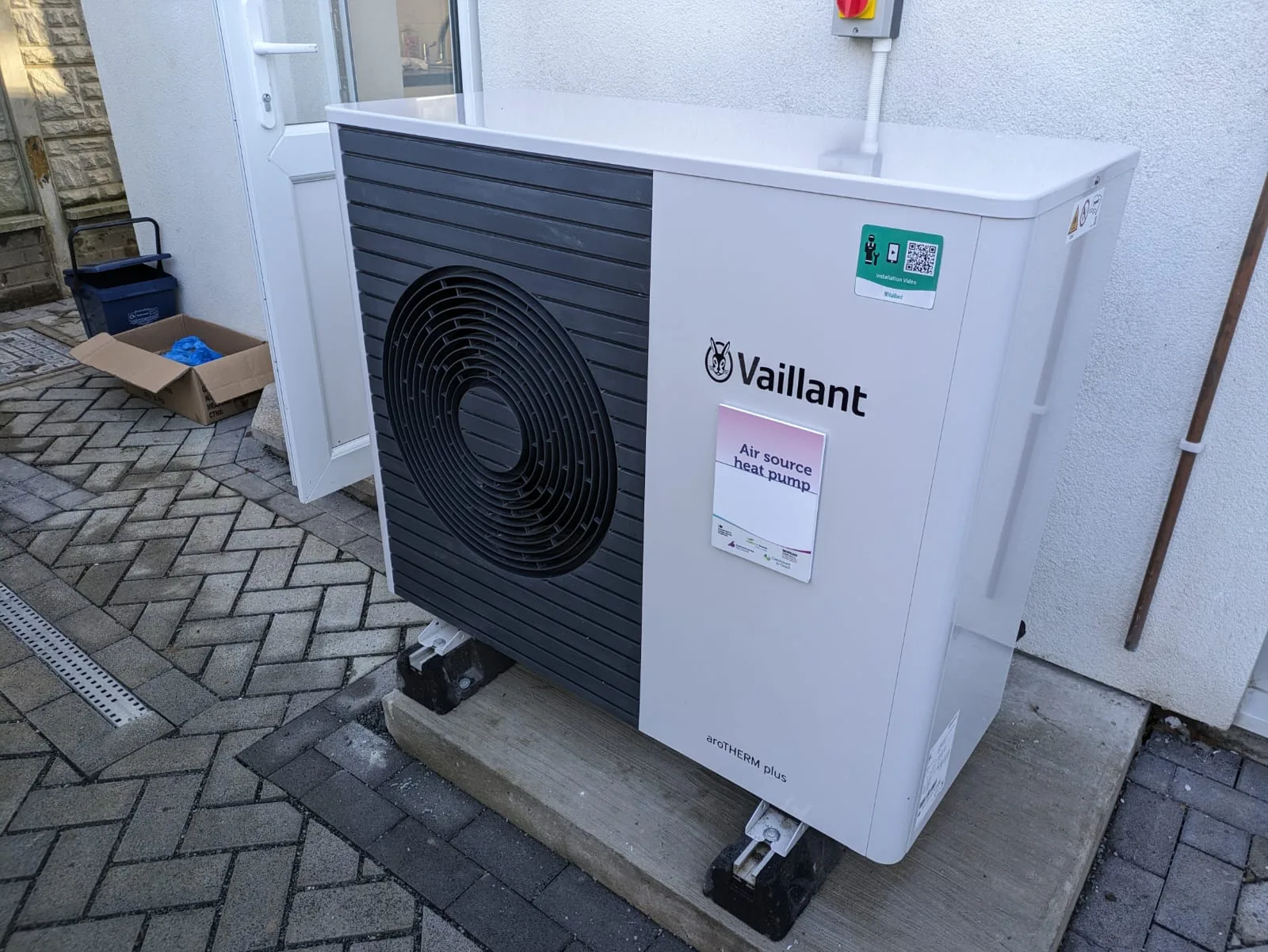 Unité extérieure de pompe à chaleur air-eau Vaillant posée sur un socle contre le mur d'une maison