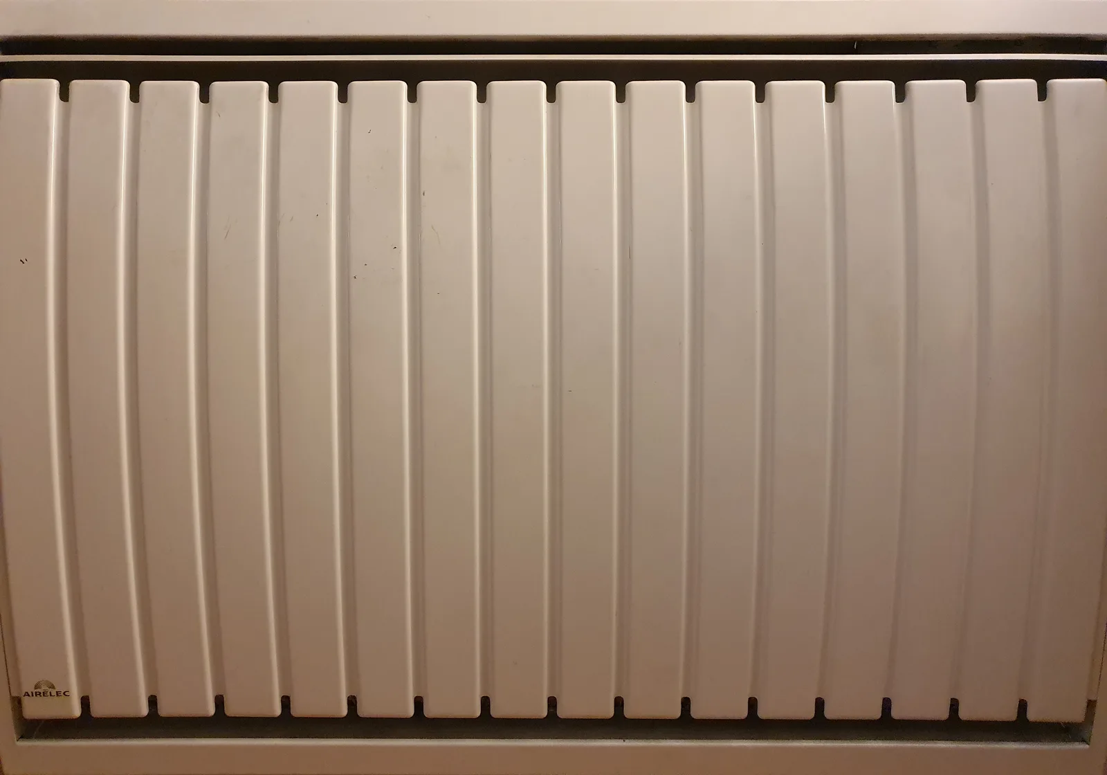 Façade d'un radiateur électrique à inertie Airelec à lames verticales blanches, installé sous une fenêtre