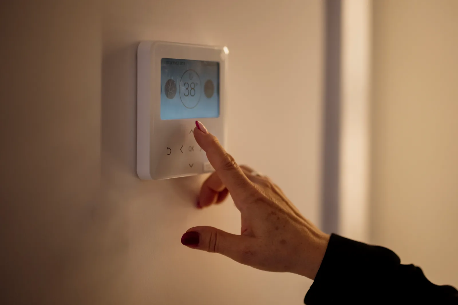 Main réglant la température sur une commande murale de chauffage à écran tactile